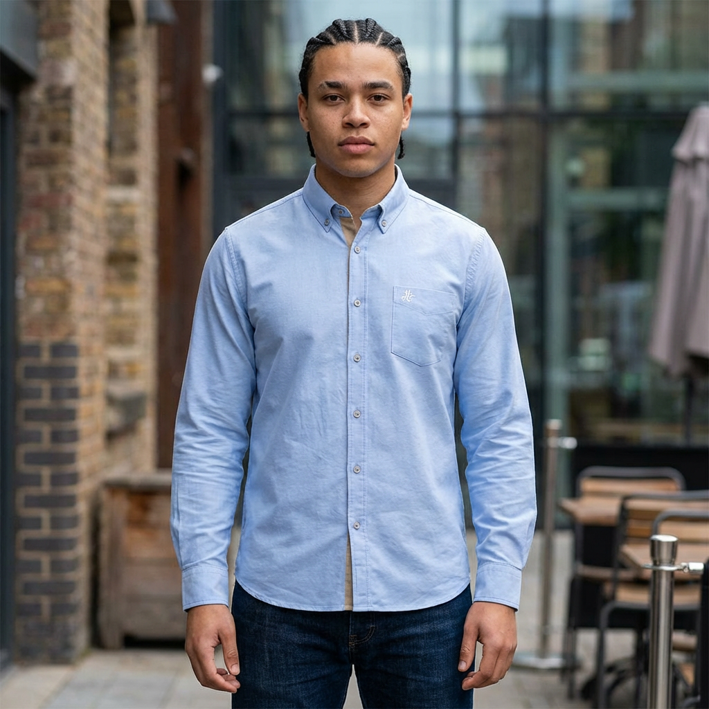 Man wearing a light blue button-up shirt standing outdoors.