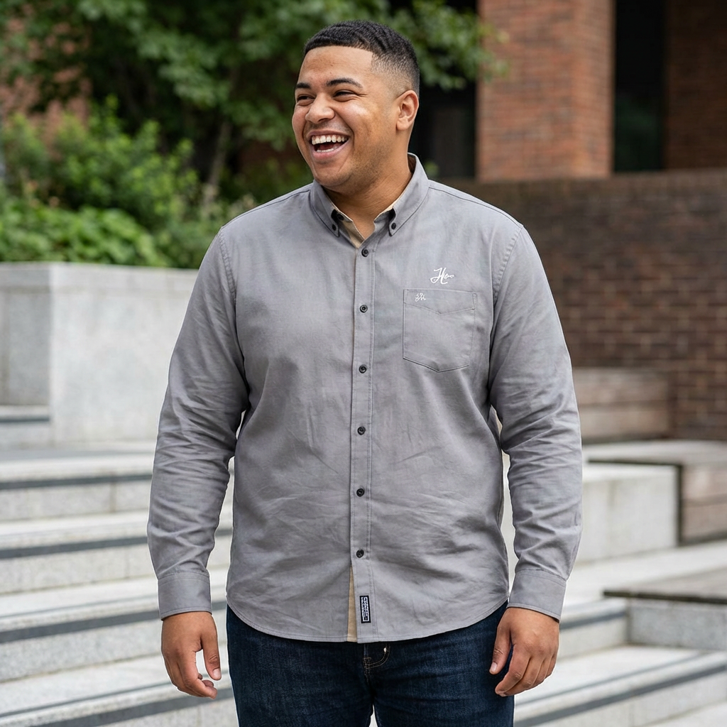 Man wearing a gray button-up shirt with a logo, standing outdoors.